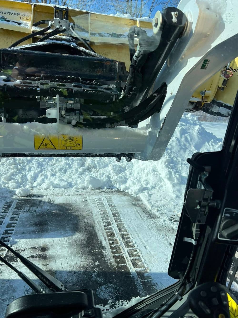 View from a snowplow cabin with snow and tire tracks on the ground.